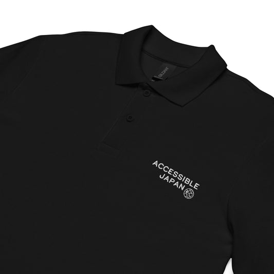 Close-up of a black polo shirt showing the "Accessible Japan" logo in white on the left chest, with a button collar.